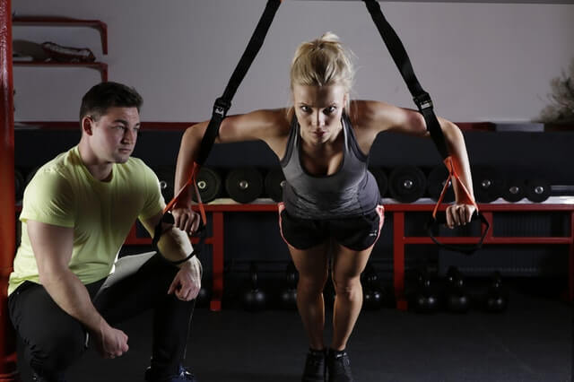 a woman performing suspension training exercises while a personal trainer supervises her form and progress. This highlights the expertise and guidance a personal trainer provides to effectively build muscle and improve strength.