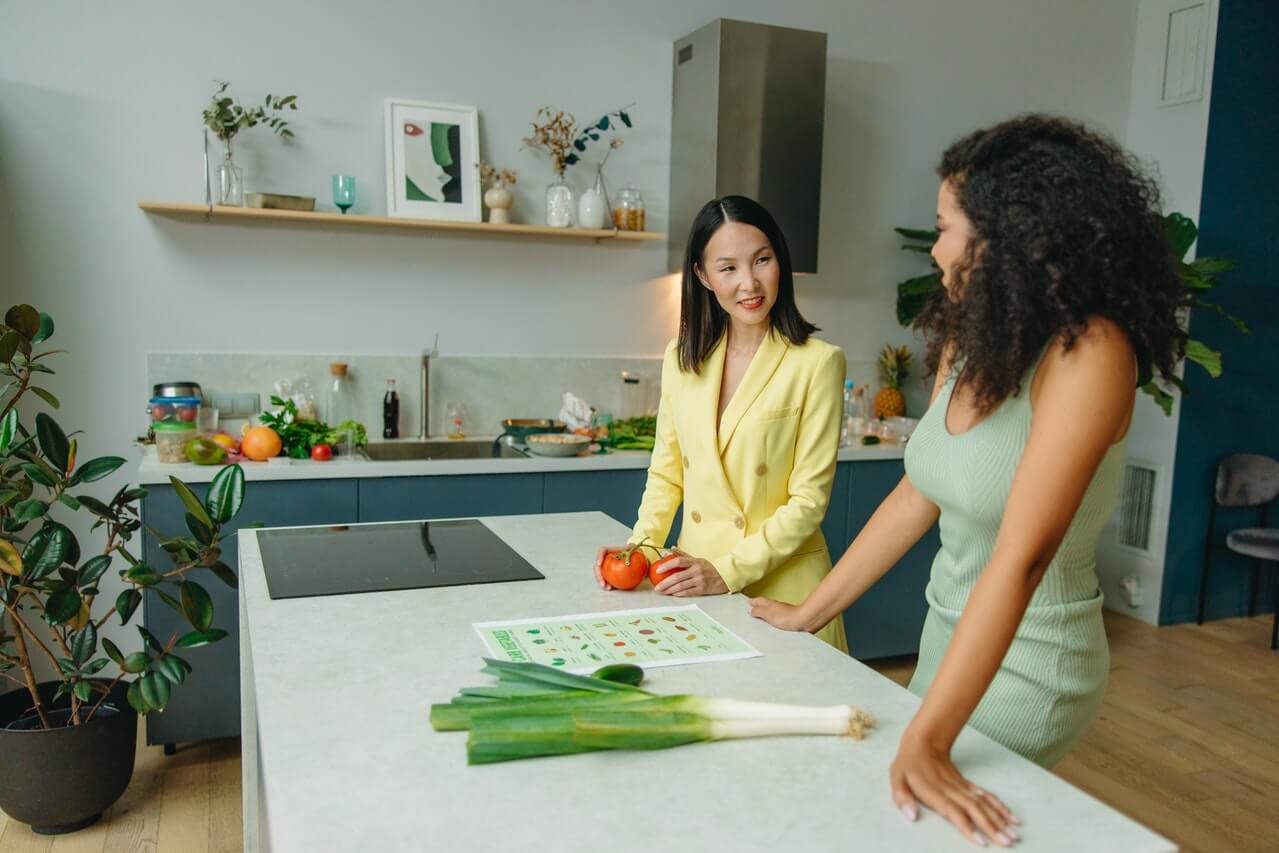 Two women discussing healthy food choices in a modern kitchen, emphasizing the importance of consulting a nutritionist for personalized dietary guidance.