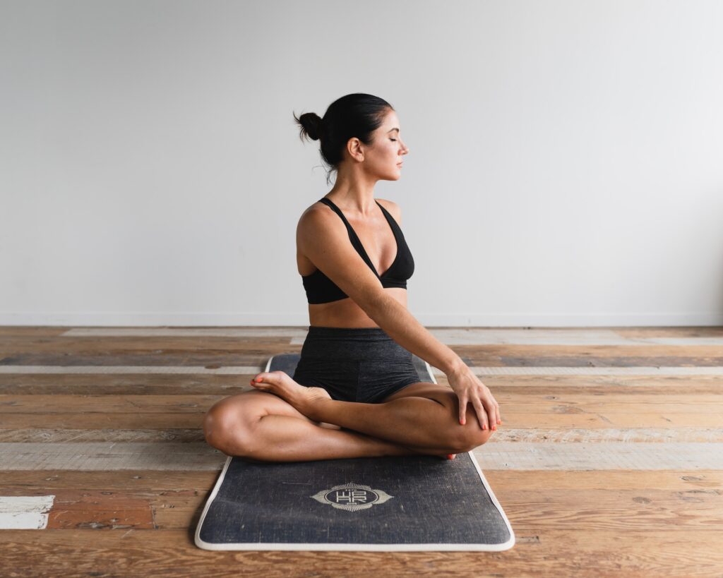 A woman performing a seated yoga pose on a mat, demonstrating the balance between yoga and strength training for a holistic fitness approach.