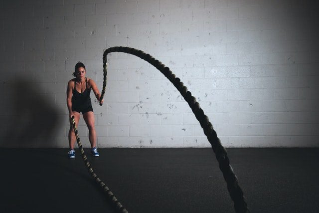 A woman using battle ropes in a gym, emphasizing the importance of avoiding common CrossFit mistakes beginners often make.