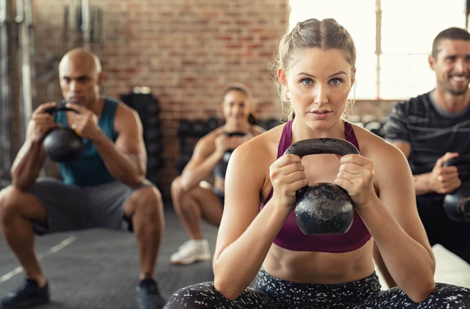Benefits of Group Fitness Classes highlighted with individuals doing kettlebell squats in a lively studio environment.