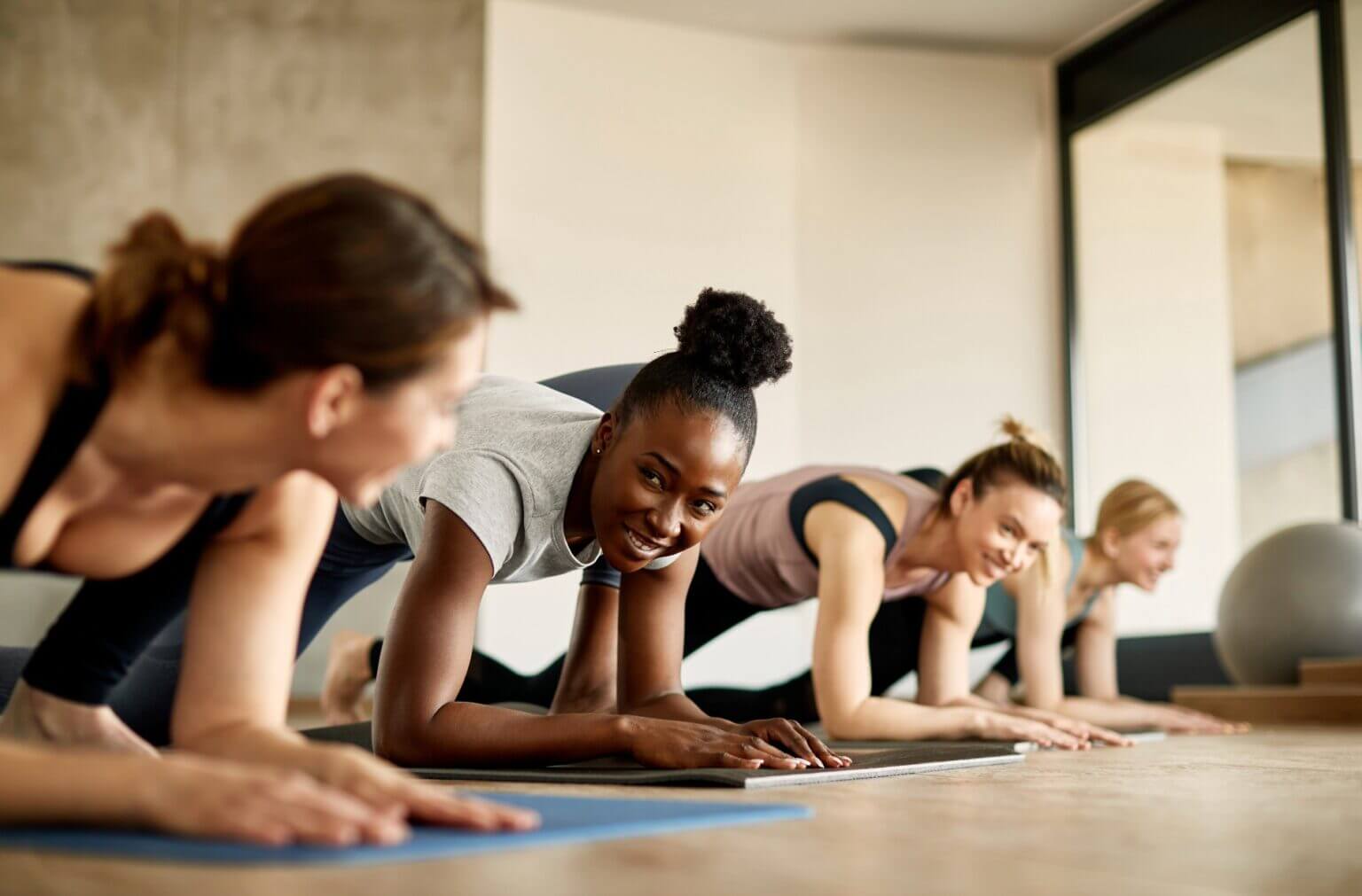 a group of women smiling and engaging in a plank exercise during a fitness class, showcasing the camaraderie, motivation, and energy-sharing benefits of group exercise classes.