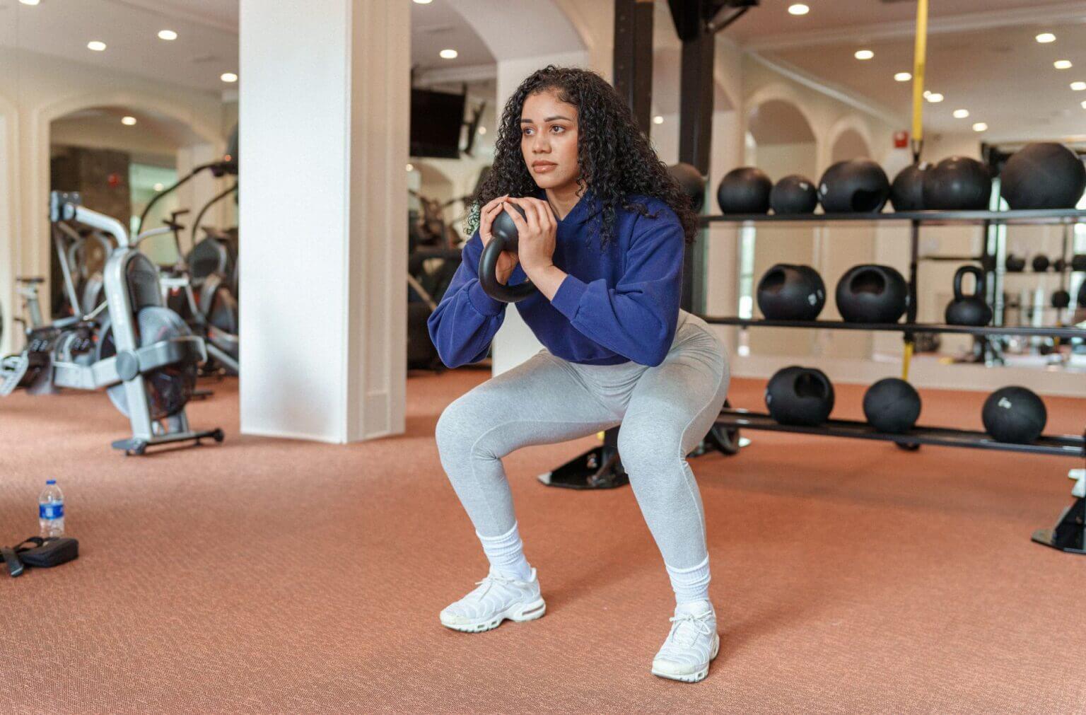 Consistent Workout Routines shown with a woman performing kettlebell squats in a well-equipped gym.