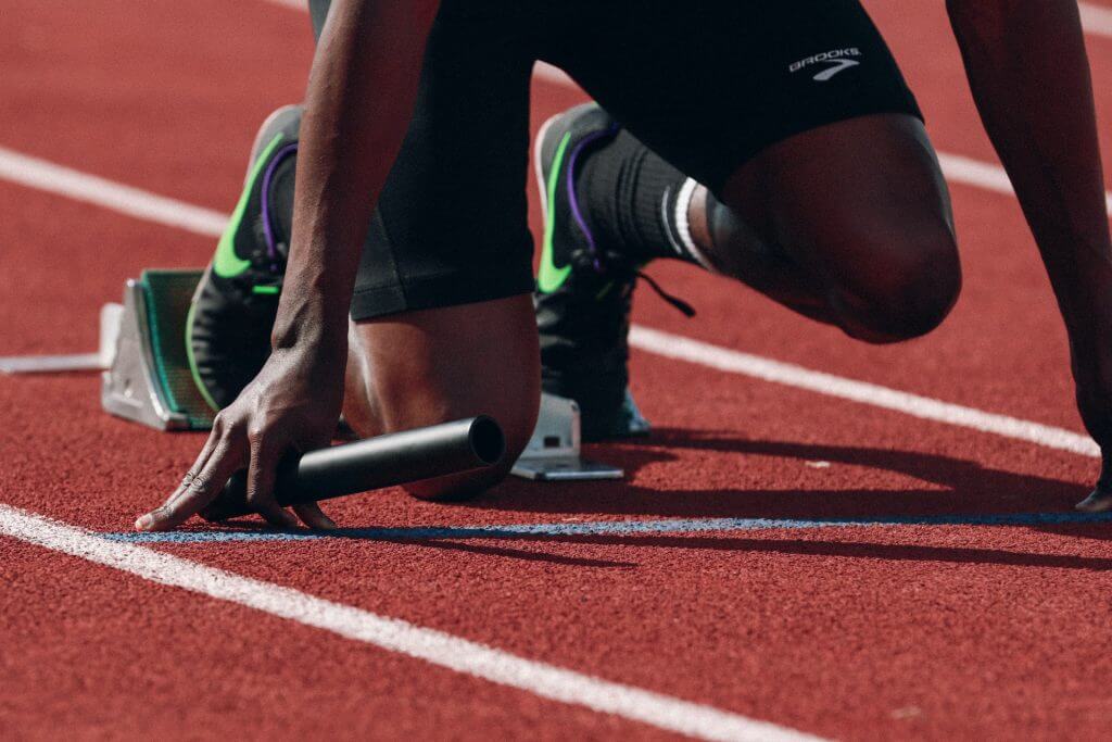an athlete at the starting line of a track, holding a baton and poised to sprint. This highlights the determination and focus required to push beyond performance limitations in elite sports.