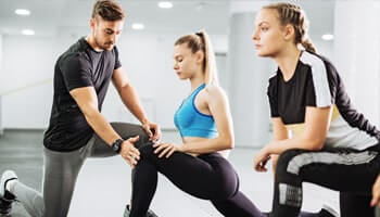 a personal trainer assisting two women in a gym setting as they perform lunges, fostering focus, guidance, and motivation. This highlights the psychological benefits of personal training, such as confidence, discipline, and stress relief.