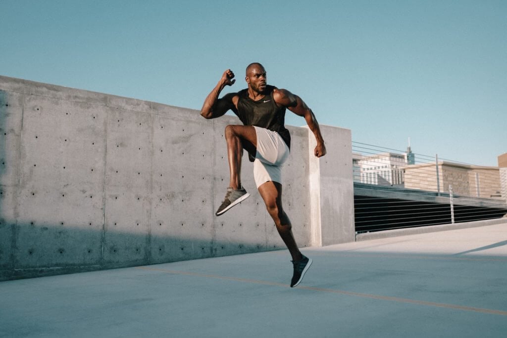 a man performing a dynamic jump in an outdoor setting, demonstrating strength and agility. It emphasizes the physical benefits and camaraderie associated with group fitness classes for men.