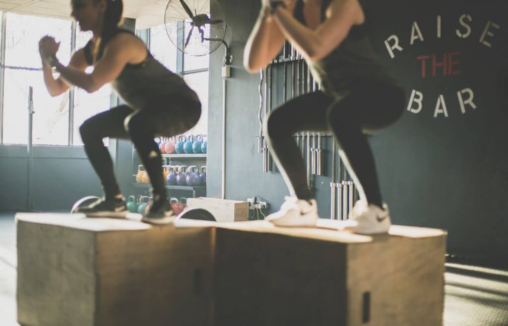 Two individuals performing box jumps under supervision, showcasing how personal trainers help adapt exercises for clients with medical conditions.