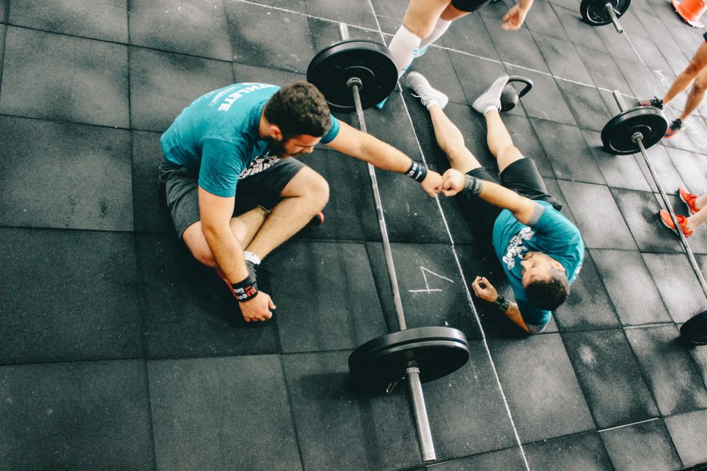 Two men supporting each other after a workout, emphasizing camaraderie and the importance of a personal trainer for seniors to ensure safe and effective training.