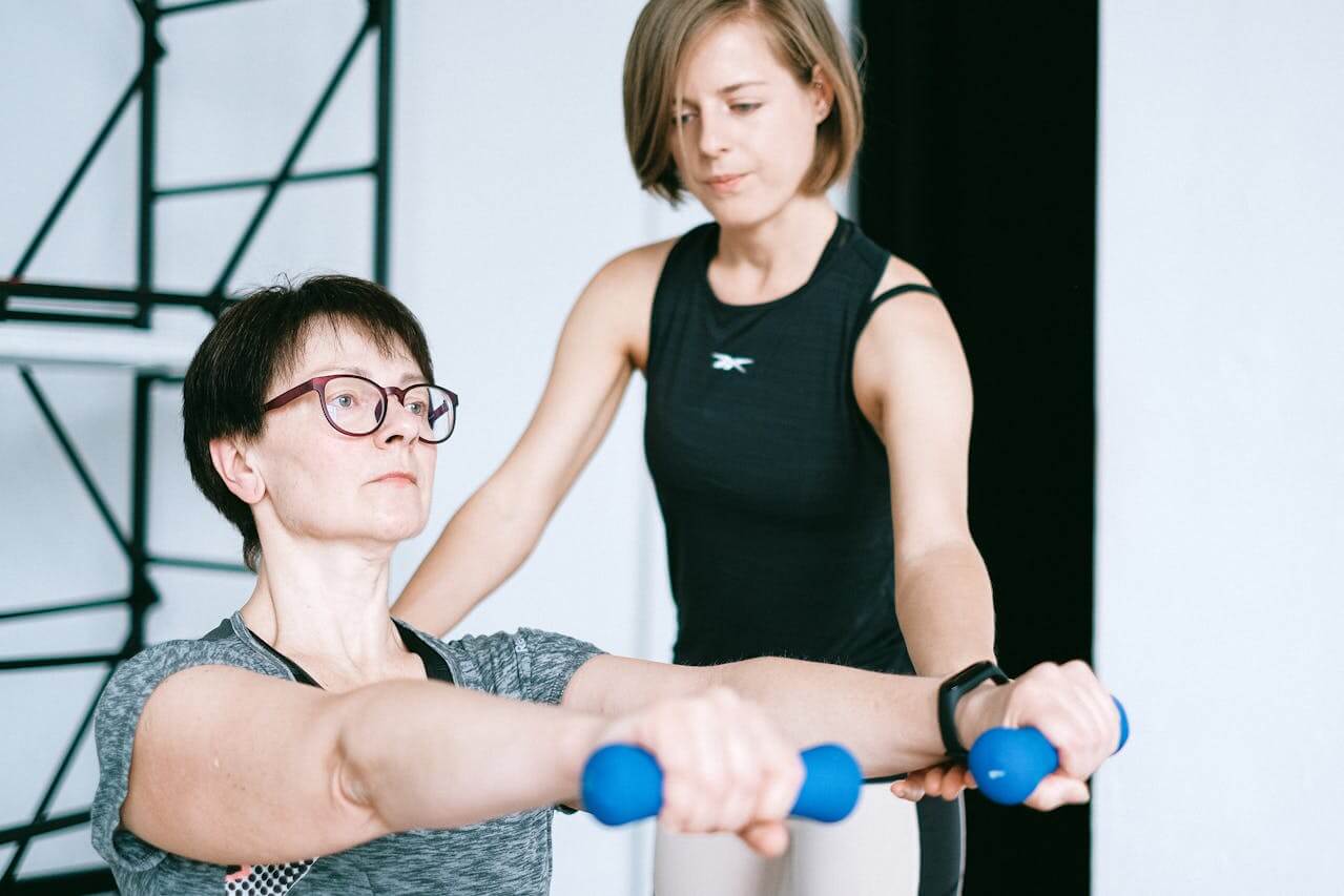 a personal trainer assisting an older woman in performing strength exercises with dumbbells, emphasizing personalized guidance and encouragement to achieve fitness goals effectively.
